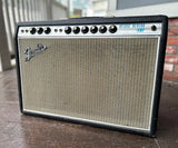 Fender deluxe reverb amplifier with black tolex, grey grill cloth on a wooden surface with a blurred background