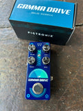 A blue Pigtronix Gamma Drive analog overdrive guitar pedal with four silver knobs and a footswitch, shown in front of its blue and black retail box on a rustic wooden surface.