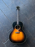 A vintage Gibson Tenor acoustic guitar with a sunburst finish, rosewood fretboard and bridge, black headstock laid flat on a dark wooden plank floor.