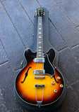 A Gibson ES-330TD sunburst electric guitar with a black body and neck, resting inside a black hard case on a dark wooden plank surface.