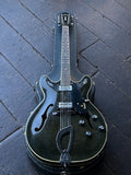 A Guild vintage twelve string guitar in dark green finish with chrome hardware, rosewood fretboard, black headstock resting on case displayed on wood floor