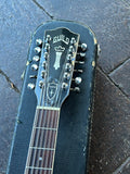 A close-up of a Guild double-headstock acoustic guitar headstock resting on a black hard case, placed on a dark stone or tile surface.