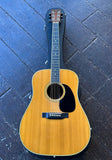 A 1972 Martin D-35 natural wood acoustic guitar with a black pickguard, rosewood fretboard,  and rosewood headstock, resting on a dark textured floor next to its black carrying case.