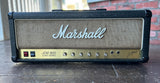 A Marshall JCM 800 Lead Series guitar amplifier head sitting on a dark wooden surface with a brick wall in the background.