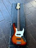 AF ender four-stringAmerican Jazz bass  guitar with a sunburst finish, resting inside a black crocodile-embossed hard case on a dark wooden plank floor.