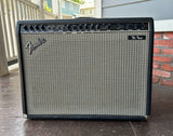 A Fender Twing amplifier with a black cabinet, silver grille, and control knobs, photographed outdoors on a tiled patio with a brick wall and railing in the background.