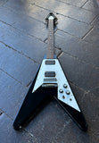 A black Gibson Flying V shape electric guitar with a V-shaped body, resting on a dark wooden plank floor.