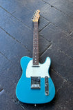 A Fender Telecaster Lake Placid Blue guitar, with white pick guard, rosewood fretboard, maple headstock resting on wooden surface