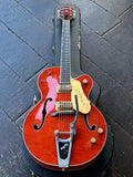 2002 Gretsch G6120TM Tiger Maple Orange finish, with gold pick ups, chrome bigsby , ebony fretboard, brown headstock on black case resting on wooden floor