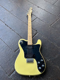 A Squier custom telecaster yellow electric guitar with a black pickguard and maple neck, photographed from above on a dark wooden plank floor.