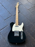A black Fender Telecaster electric guitar with a cream pickguard and maple neck, photographed from above on a dark wooden plank floor.