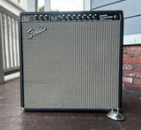 A Fender Super Reverb Amp combo amplifier with a silver grille and black frame, photographed outdoors on a porch with a brick wall and siding in the background.