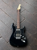 A 2011 Fender Stratocaster Blacktop model, black electric guitar with a glossy finish, chrome hardware and pick ups, rosewood fretboard, resting diagonally on dark wooden planks.