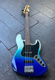 A Fender Jazz bass four-string electric bass guitar with a glossy blue-to-white gradient finish, resting on a dark gray wooden plank floor.
