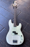 A white Fender electric precision bass guitar with a dark brown neck and black hardware, photographed from above on a dark wooden plank floor.