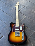 A Fender Telecaster electric guitar sunburst with a classic sunburst finish, resting on a dark gray wooden plank floor.