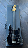 A black ender fretless electric bass guitar with a maple  headstock, resting inside an open black hard case on a dark gray tiled floor.