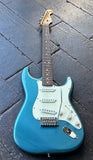 A Squier Stratocaster blue electric guitar with a white pickguard and silver hardware, resting on a dark wooden plank floor.