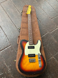 Electric guitar with sunburst finish in a brown case on a wooden floor.