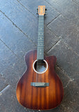 A Martin cutaway acoustic guitar with a warm brown wood finish, resting on a dark wooden plank floor.