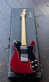 A wine red Fender Telecaster reissue 70's electric guitar resting inside a black hard case on a dark wooden floor.