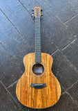 Taylor GS Mini koa acoustic guitar with and dark neck, photographed from above on a dark stone tile floor.