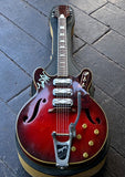 A red Silvertone electric guitar with  three pick ups , silver and a black headstock, resting on a circular display stand over a dark wooden plank floor.