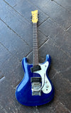 A blue Morales electric guitar with a white pickguard, two black pick ups, metal tremolo  and yellow headstock, photographed from above on a dark wooden plank floor.