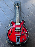 A red electric Univox hollow-body guitar with bigsby guitar with a black hard case, photographed from above on a dark wooden floor.