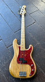 A Custom four-string bass guitar with a natural wood body, maple neck, and a red speckled pickguard, photographed on a dark wooden plank floor.