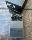 black Boss Metal Zone MT-2 effects pedal on a textured surface with packaging in the background.
