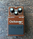 A Boss Octaver OC-2 guitar effects pedal with a metallic copper-brown body, black knobs, and a black footswitch, photographed on a textured dark surface.