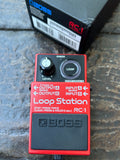 A red and black Boss RC-1 Loop Station guitar effects pedal placed on a stone surface, with the original black product box partially visible behind it.
