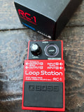 A Boss RC-1 Loop Station guitar effects pedal in red and black, shown with its black RC-1 box on a dark wooden surface.