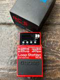 Red Boss Loop Station RC-5 pedal on a wooden surface with its packaging in the background.