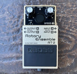 A Boss Rotary Ensemble RT-2 guitar effects pedal with a cream-colored metal casing, black faceplate, and silver knobs, resting on a textured dark gray surface.