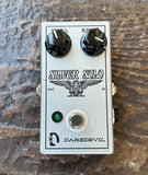 A silver metal guitar effects pedal with black knobs, labeled 'SILVER SOLO' and 'DAREDEVIL', placed on a textured brown surface.