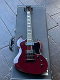 Adark red electric guitar with a black pick-guard and silver hardware, resting on top of a black guitar case on a gray stone patio. ESP LTD E-II