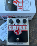 Electro-Harmonix Big Mufflade guitar effects pedal in front of its original white and red retail box, displayed on a dark wooden tabletop.