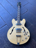 A natural wood Epiphone double-cutaway electric guitar with chrome hardware, photographed from above on a dark blue wooden floor.