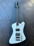 An Alpine White Epiphone Thunderbird electric bass guitar with a dark fretboard and black pickups, resting inside a black hard case on a dark wooden plank floor.