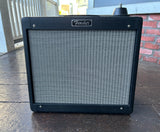 Black tolex Fender guitar amplifier on a wooden deck with a brick wall in the background