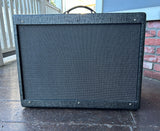 A Fender Hotrod deluxe amplifier dark grey textured guitar amplifier speaker cabinet with grey grille cloth and top handle, photographed outdoors on a wooden deck against a brick wall.