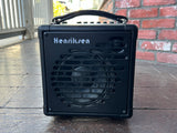 Black portable speaker with 'Henriksen' branding on a wooden floor.