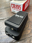 Black guitar pedal with 'cry baby branding on a wooden surface, with a box labeled 'CBJ95' in the background.
