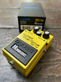 Yellow Boss SD-1W Super Overdrive pedal on a wooden surface with a black box in the background.