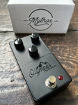Black effect pedal with 'Olympus Overdrive' branding on a wooden surface, with a white box labeled 'Mythos' in the background.