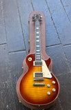 A Gibson Les Paul Custom electric guitar in a brown sunburst finish, resting inside its brown hard case on a dark gray wooden deck.