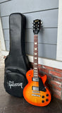 Full shot of 2022 Gibson Les Paul Studio Tangerine Burst upright next to included gig bag
