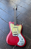 A red danelectro electric guitar with a gold pickguard and silver control plate, resting on a dark wooden plank floor.
